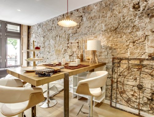 Découvrez les objets déco et arts de la table au showroom Bulles Cuisines à Lyon, fraîchement rénové. Table bois avec pied en métal, tabouret bois avec revêtement blanc tendance scandinave, mur en pierres apparentes.